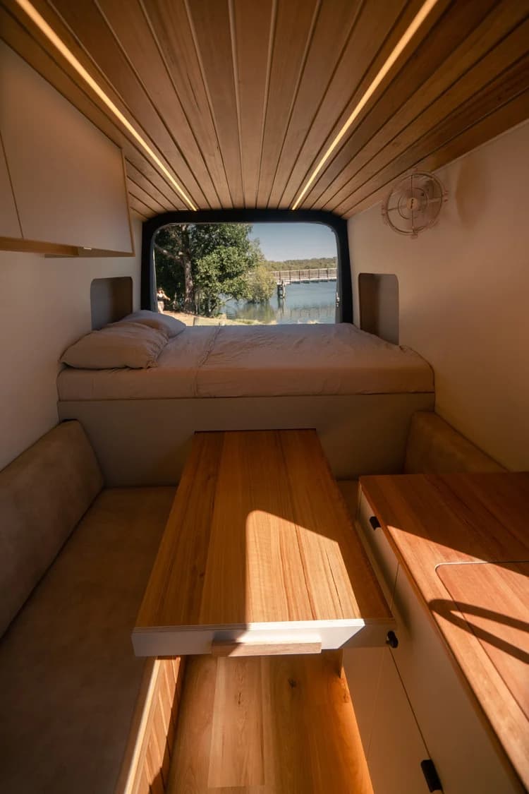 The bed and pull-out table inside the campervan, with trees and water through the rear window