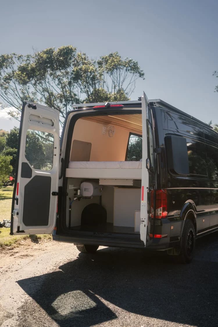 The deep-purple campervan on grass with its rear doors open to the bed