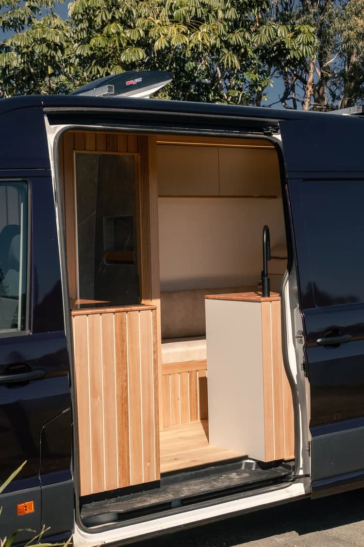 Side sliding door of the deep-purple campervan open, showing timber cabinetry inside