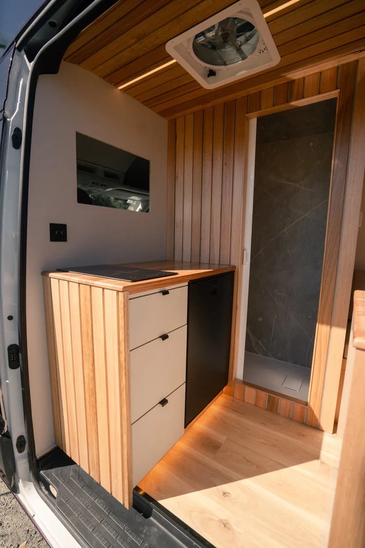 Galley with twin induction cooktop, timber benchtop and 95L fridge beside the shower door