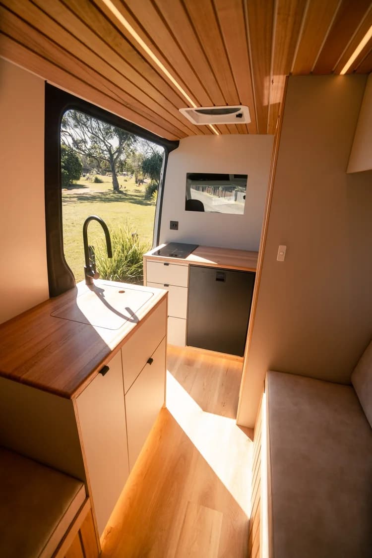 Galley with sink, cooktop and fridge below a window looking onto parkland