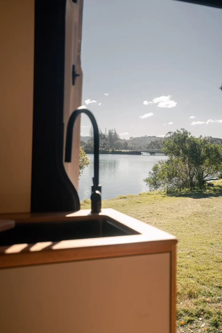 Looking out from the campervan galley across grass to a river and timber jetty