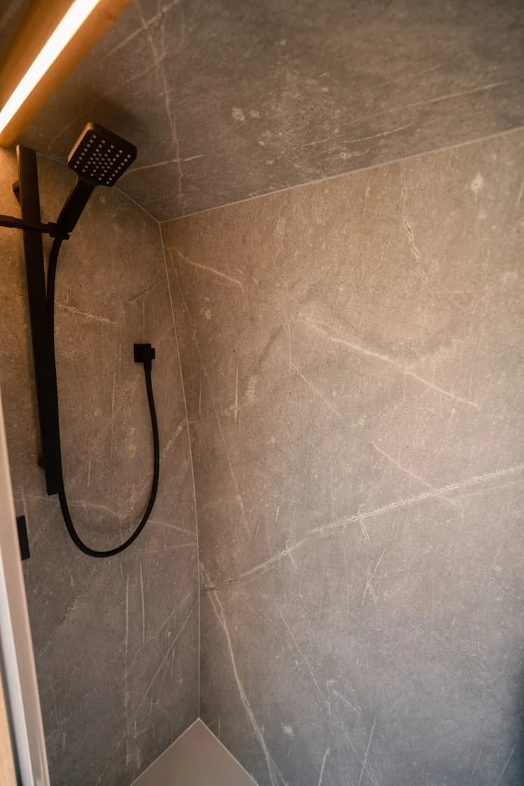 Private shower finished in honed stone with a black handheld showerhead